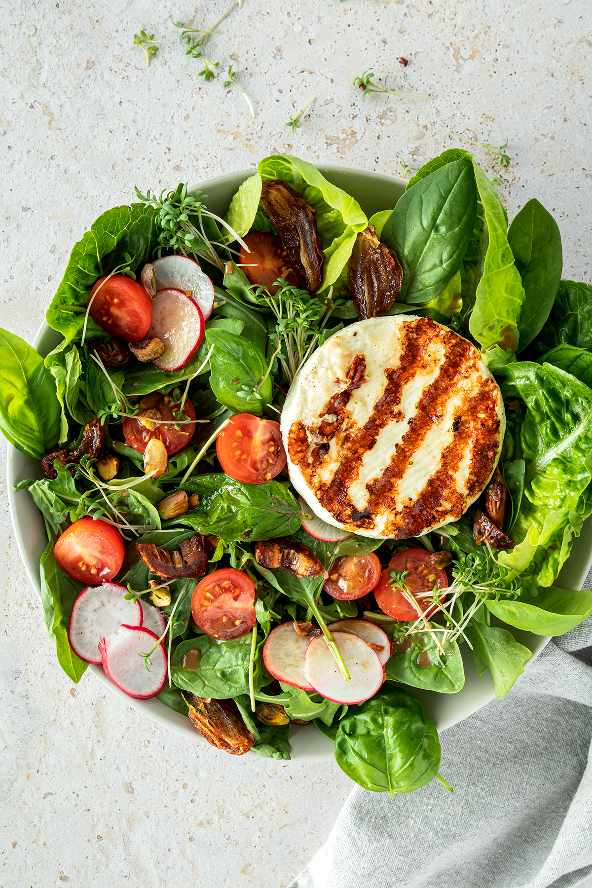 Salat Bowl mit Grillk&auml;se, Cherrytomaten, Datteln, d&uuml;nnen Radieschen Scheiben und N&uuml;ssen.
