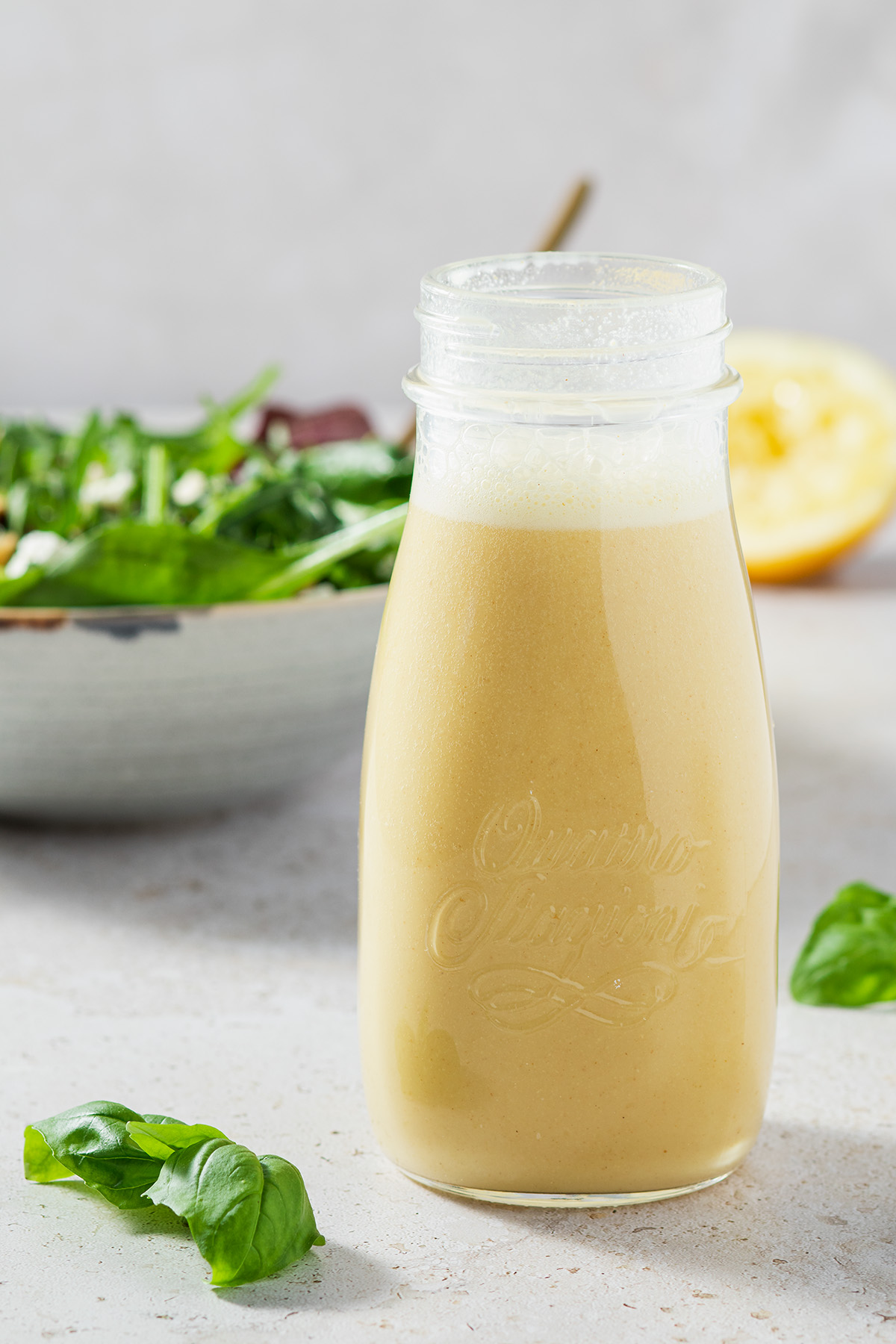 Salatdressing in einer Glasflasche, im Hintergrund eine Salatsch&uuml;ssel und eine halbe Zitrone