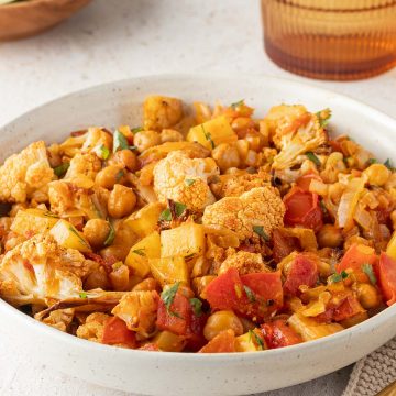 Blumenkohl Kartoffel Curry mit Kichererbsen in einem Teller, Deko im Hintergrund.