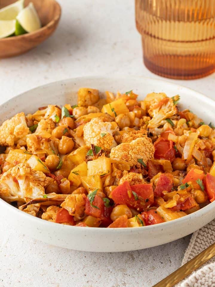 Blumenkohl Kartoffel Curry mit Kichererbsen in einem Teller, Deko im Hintergrund.
