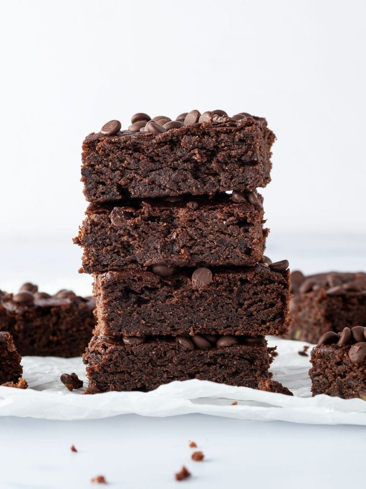 Ein Stapel aus vier saftigen Avocado Brownies, mit weiteren Brownies im Hintergrund.