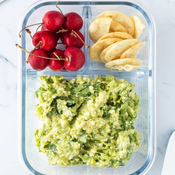 Avocado Eier Salat in einer Lunchbox mit Crackern und Kirschen, Scheibtisch-Gegenstände liegen im Bildrand.