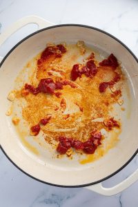 Knoblauch, Sirup und Tomatenmark werden in einer Pfanne angebraten.