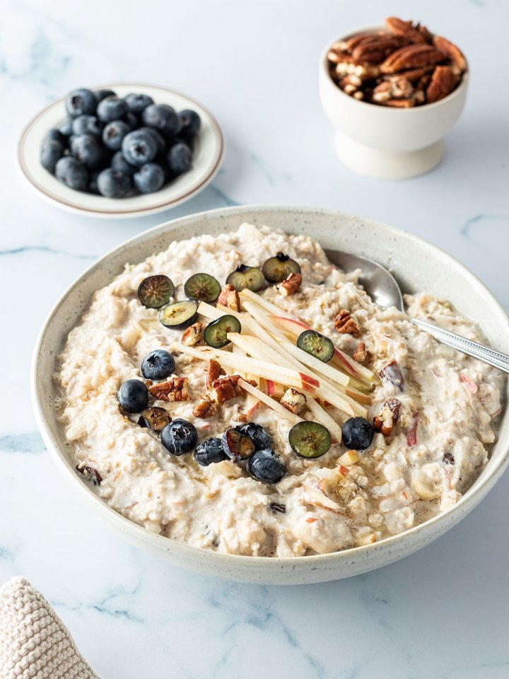 Bircher Müsli mit frischem Obst und Nüssen in einer Schüssel, frische Blaubeeren und Nüsse im Hintergrund.