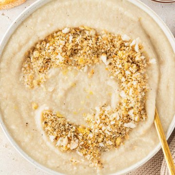 Vogelperspektive auf einen Teller Blumenkohlsuppe serviert mit einem knusprigen Brotkr&uuml;mel-Topping, Deko im Bildrand.