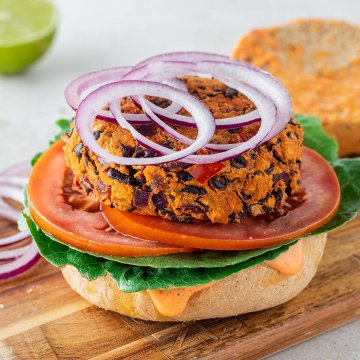 Bohnenbratling auf einem Burgerbr&ouml;tchen mit frischem Salat, Tomatenscheiben und Zwiebelringen.