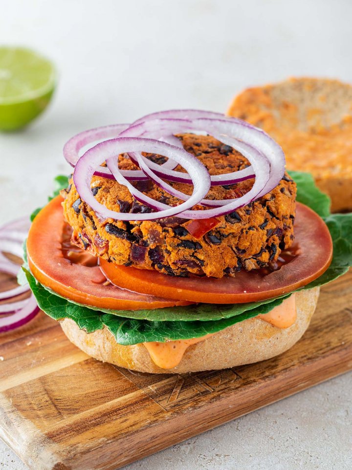 Bohnenbratling auf einem Burgerbr&ouml;tchen mit frischem Salat, Tomatenscheiben und Zwiebelringen.