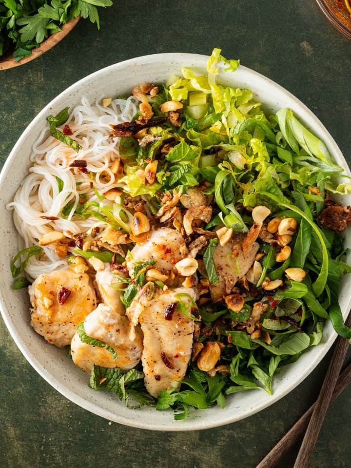 Eine Sch&uuml;ssel Bun Tron, ein vietnamesischer Reisnudelsalat mit frischen Kr&auml;utern, Salat, H&auml;hnchen und knusprigen Erdn&uuml;ssen, auf einem dunkelgr&uuml;nen Untergrund.