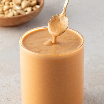 Cremiges Cashew-Dressing in einem Glas, mit einem Löffel und Cashews im Hintergrund.