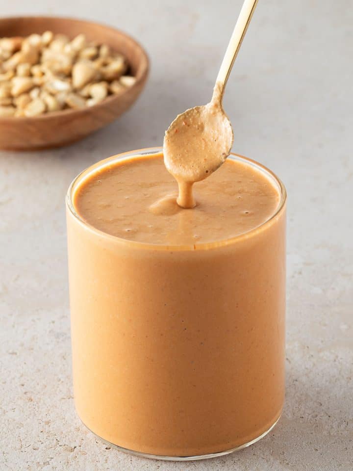 Cremiges Cashew-Dressing in einem Glas, mit einem L&ouml;ffel und Cashews im Hintergrund.