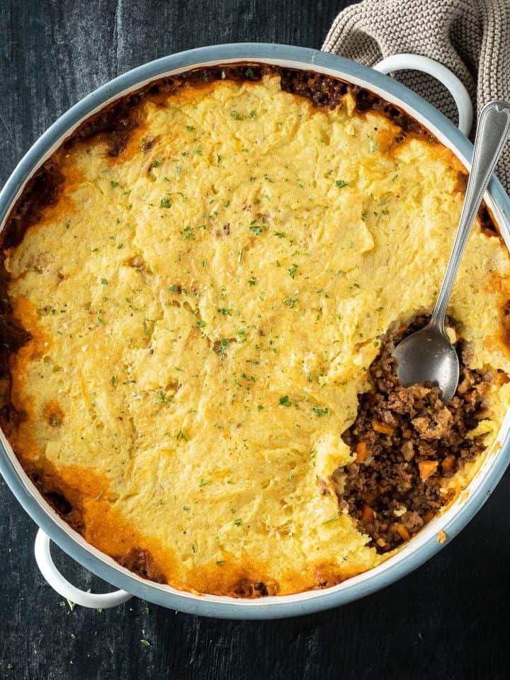 Cottage Pie in einer gro&szlig;en runden Auflaufform, wo eine Portion rausgenommen wird.
