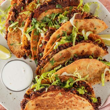 Teller mit knusprigen Crispy Tacos mit schwarzen Bohnen, Salat und Dip von oben fotografiert.