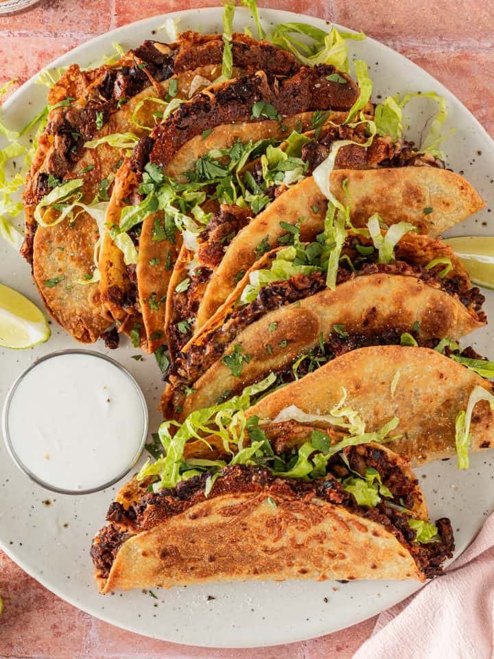 Teller mit knusprigen Crispy Tacos mit schwarzen Bohnen, Salat und Dip von oben fotografiert.