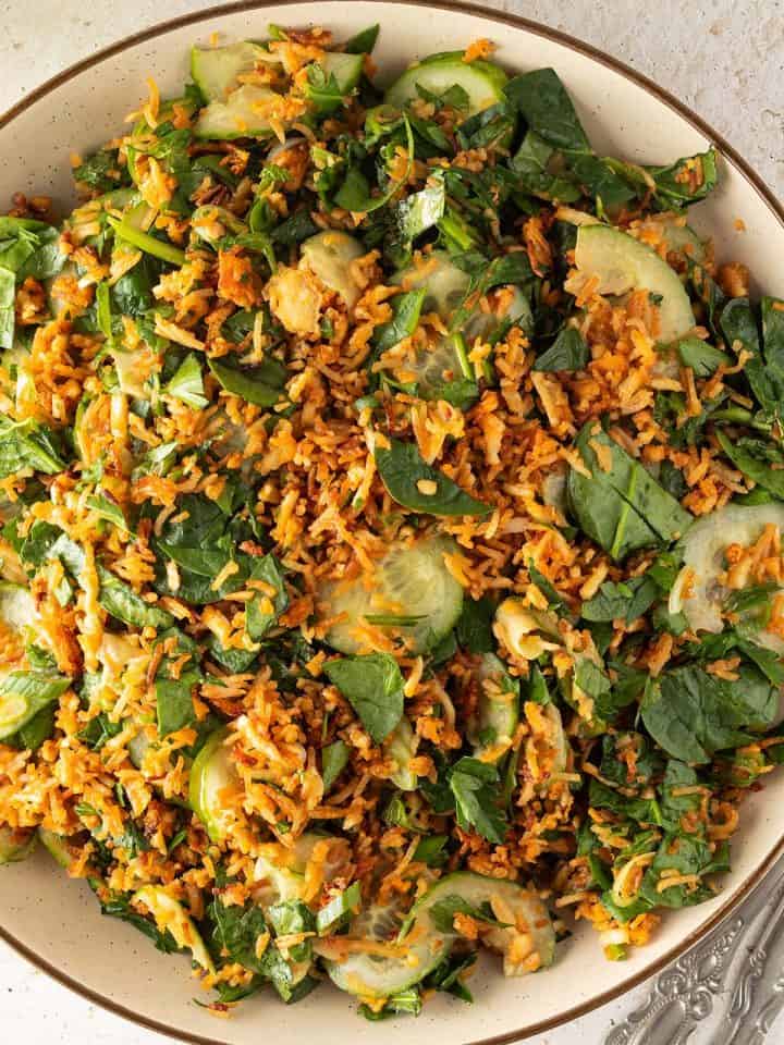 Knuspriger Reissalat mit Gurke, Spinat, Kräutern und Erdnussdressing auf einem großen Teller.