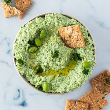 Edamame Dip in einer Schüssel, serviert mit Crackern und frischer Petersilie.