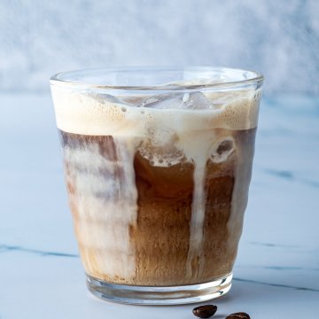 Einfache Eiskaffee aus kalt gesch&uuml;tteltem Espresso und einem Schuss Milch in einem Glas vor grau-blauem Hintergrund.
