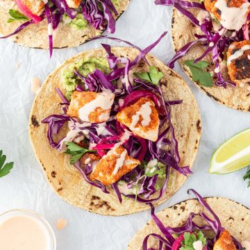 Vier mexikanische Fisch-Tacos auf weißem Untergrund mit Limetten und Sauce.