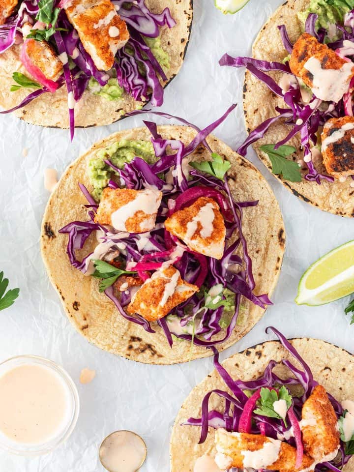 Vier mexikanische Fisch-Tacos auf wei&szlig;em Untergrund mit Limetten und Sauce.