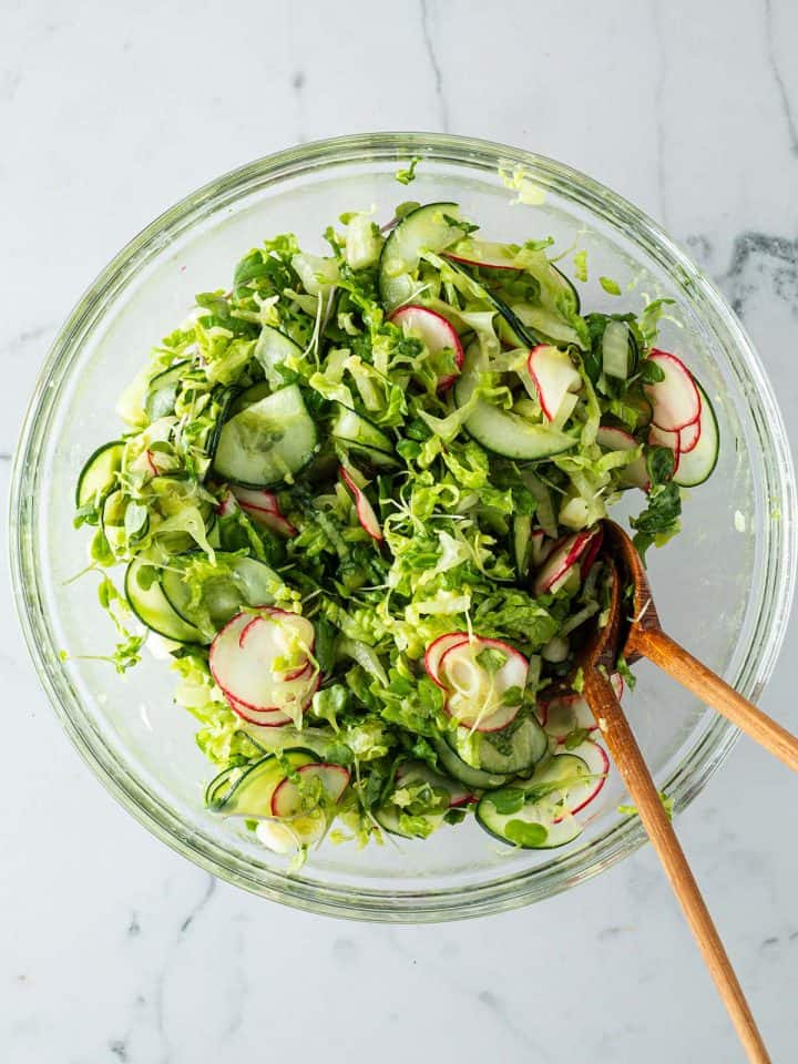Gemischter Beilagensalat mit Gurken, Salat, Radieschen in einer gro&szlig;en Glassch&uuml;ssel mit Salatbesteck.