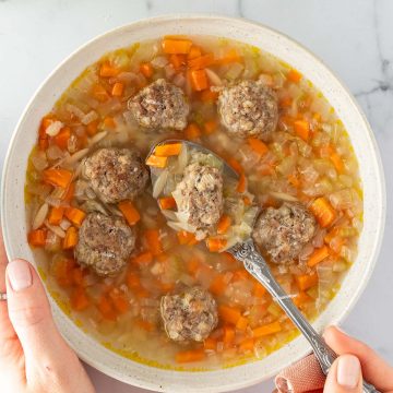 Eine Person h&auml;lt eine Sch&uuml;ssel mit Gem&uuml;sesuppe, Hackb&auml;llchen und Nudeln in der Hand.
