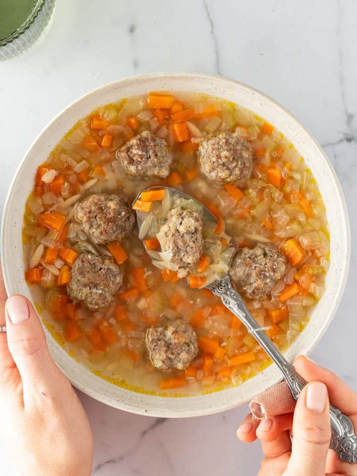 Eine Person h&auml;lt eine Sch&uuml;ssel mit Gem&uuml;sesuppe, Hackb&auml;llchen und Nudeln in der Hand.