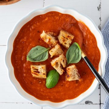 Sch&uuml;ssel mit cremiger Tomatensauce serviert mit Croutons und Basilikum, Deko im Bildrand.
