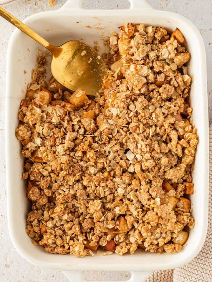 Vogelperspektive auf eine Auflaufform mit einem Apfel Crumble, aus dem bereits eine kleine Portion rausgenommen wurde.