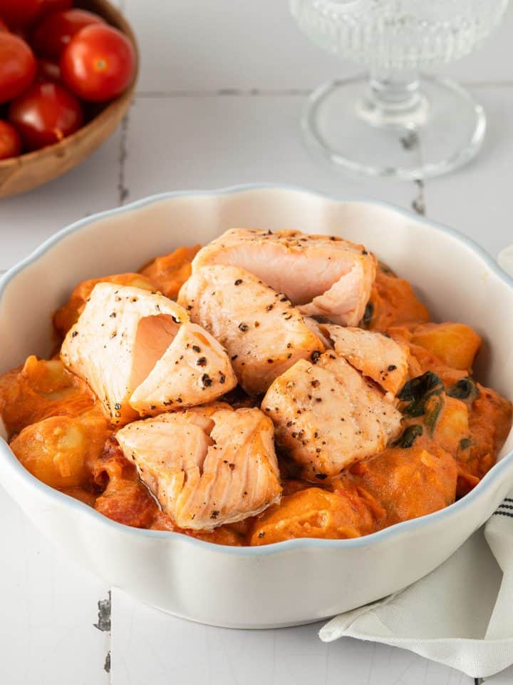 Cremige Gnocchi mit Lachs in tomatiger Marry Me Sahnesauce, angerichtet in einer wei&szlig;en Sch&uuml;ssel auf hellem Untergrund.