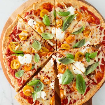 Eine Hand nimmt ein Stück von einer großen Pizza mit High Protein Pizzateig weg.