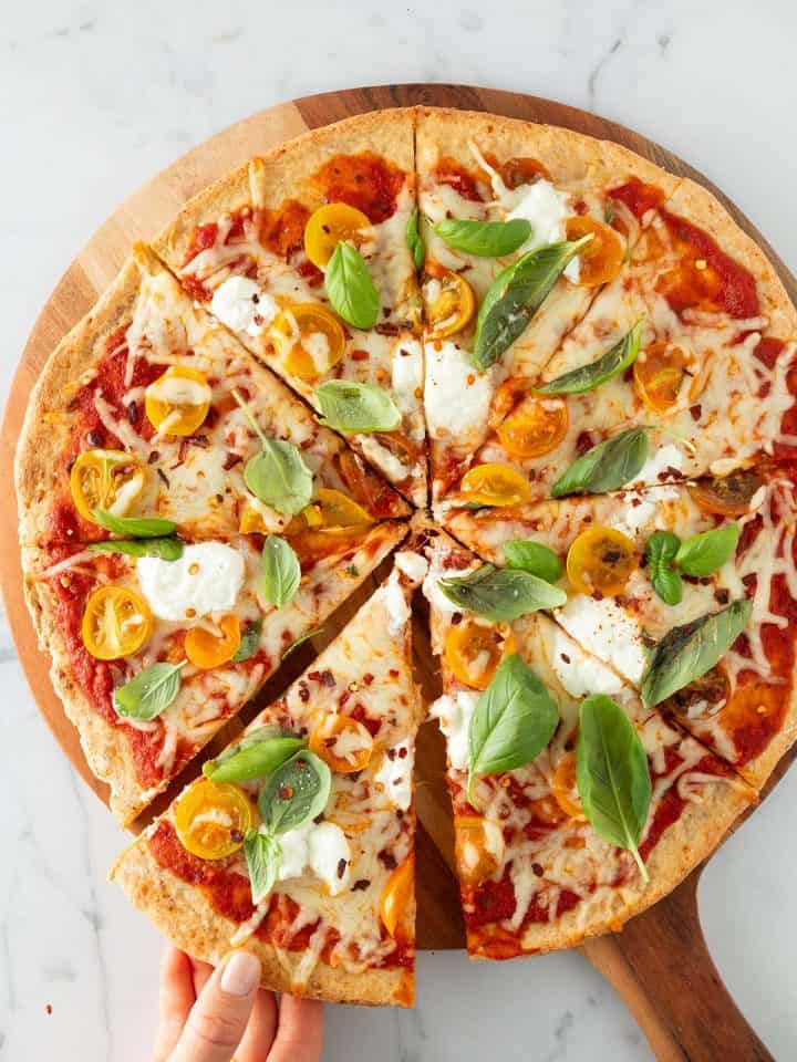 Eine Hand nimmt ein Stück von einer großen Pizza mit High Protein Pizzateig weg.