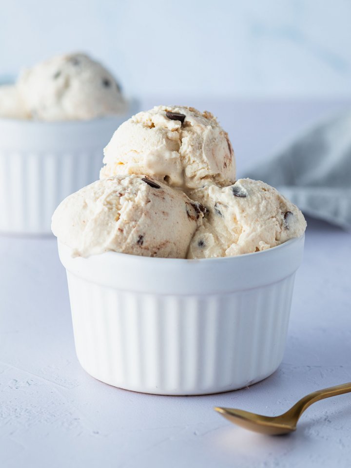 Mehrere Cottage-Cheese-Eis-Kugeln mit Schokostückchen in einer weißen Schüssel, im Hintergrund eine zweite Schüssel mit Eiskugeln.