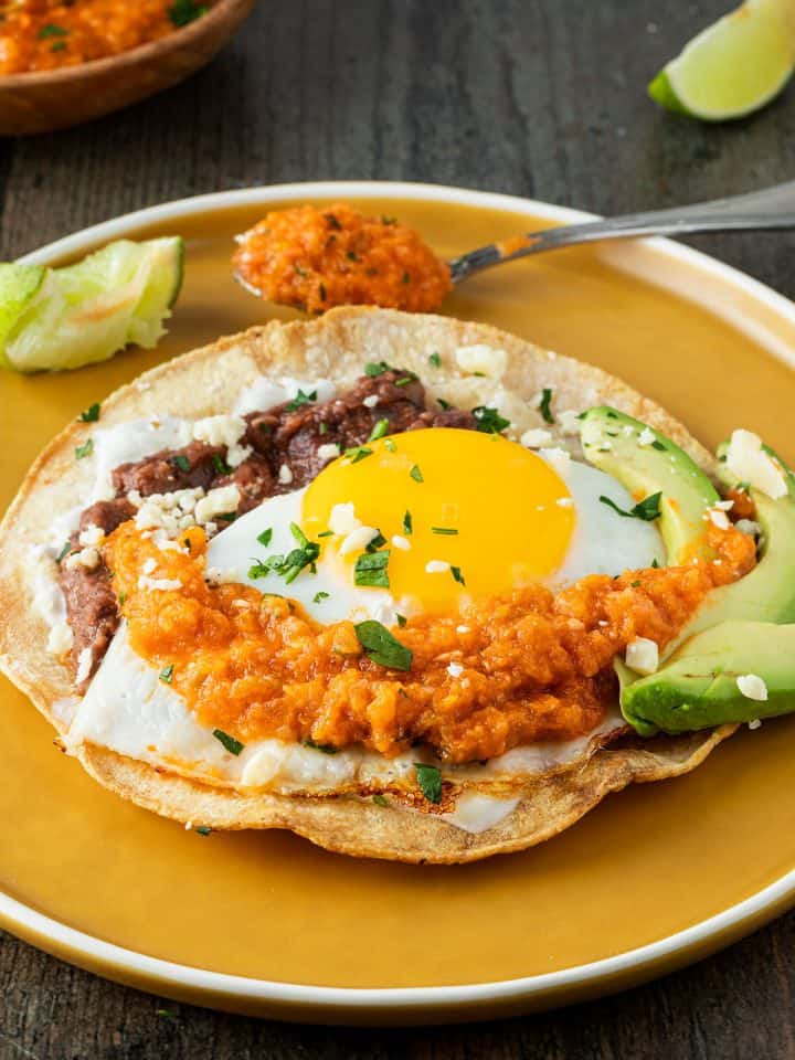 Knuspriger Tortilla mit Bohnenmus, Spiegelei und Salsa auf einem Teller.
