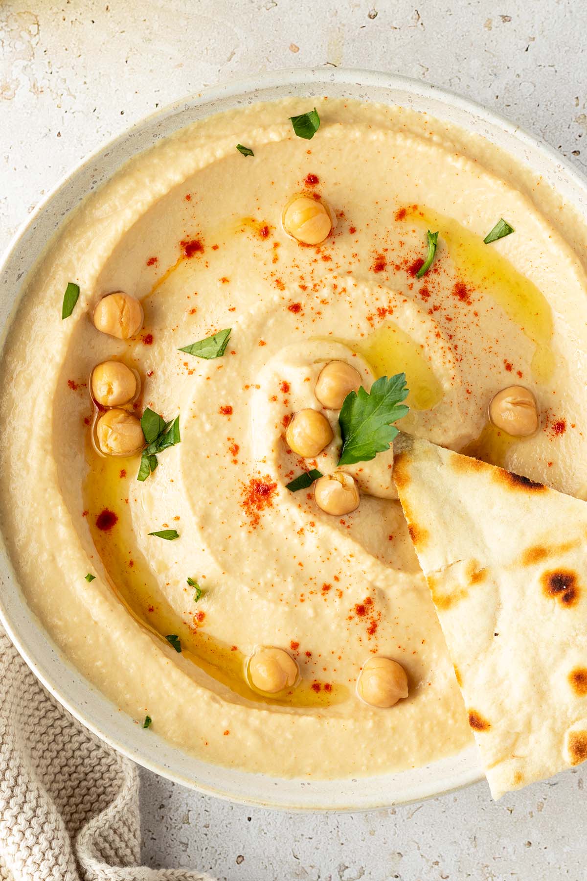 Eine Schüssel mit cremigen Hummus dekoriert mit ganzen Kichererbsen und frischen Kräutern.