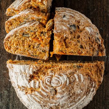 Vogelperspektive auf ein saftiges, teils aufgeschnittenes Karottenbrot, das auf einem rustikalen Holzuntergrund liegt.