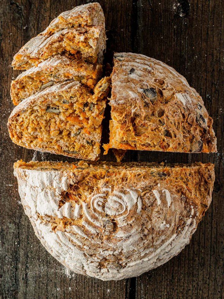 Vogelperspektive auf ein saftiges, teils aufgeschnittenes Karottenbrot, das auf einem rustikalen Holzuntergrund liegt.