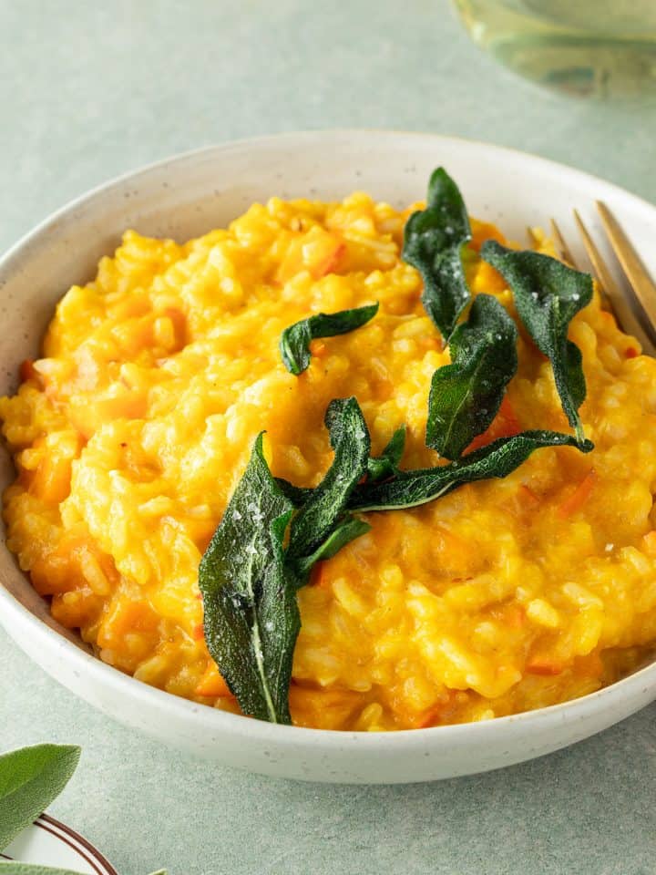 Teller mit cremigem Kürbisrisotto und mit knusprigen Salbei, Deko im Bildrand.