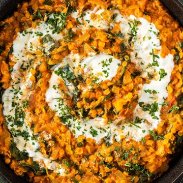 Nahaufnahme von einem Linsen Dal mit Spinat, da in einer Pfanne mit Joghurt und frischen Kr&auml;utern serviert wird.