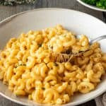 Ein Teller Mac and Cheese mit einem L&ouml;ffel, im Hintergrund ein Teller Brokkoli.