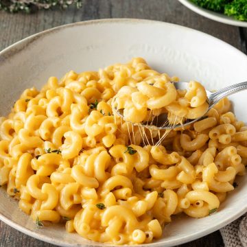 Ein Teller Mac and Cheese mit einem Löffel, im Hintergrund ein Teller Brokkoli.