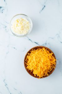 Eine Schüssel mit geriebenem Parmesan und eine Schüssel mit geriebenem Cheddar Käse.