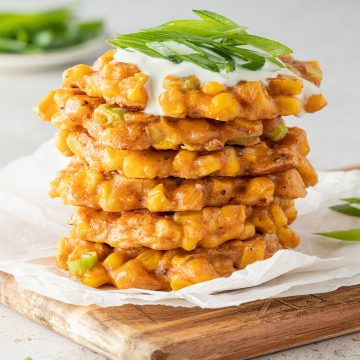 Ein Stapel aus knusprig angebratenen Maispuffern mit Sourcream und Frühlingszwiebeln on top.