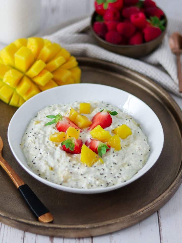 Eine Schüssel Overnight Oats mit Mango und Erdbeeren, Deko im Hintergrund.