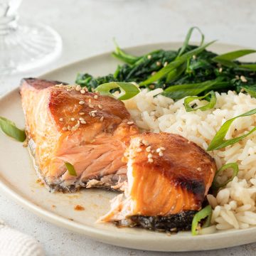 Zart gegarter Miso Lachs serviert mit Reis und grünem Blattgemüse auf einem Teller.