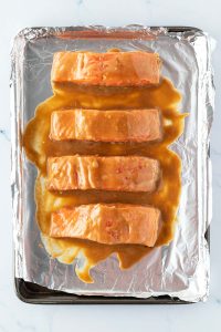 Vier mit Miso marinierte Lachsfilets auf ein mit Alufolie ausgelegtes Blech vor dem Rösten im Ofen.