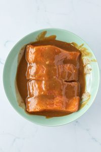 Vier rohe Lachsfilets in einem Teller, die mit der Miso-Marinade bedeckt sind.