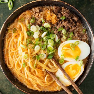 Eine Sch&uuml;ssel Miso Ramen mit Eiern, Fr&uuml;hlingszwiebeln und Hackfleisch auf einem dunkelgr&uuml;nen Untergrund.