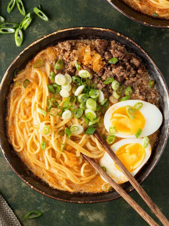 Eine Sch&uuml;ssel Miso Ramen mit Eiern, Fr&uuml;hlingszwiebeln und Hackfleisch auf einem dunkelgr&uuml;nen Untergrund.