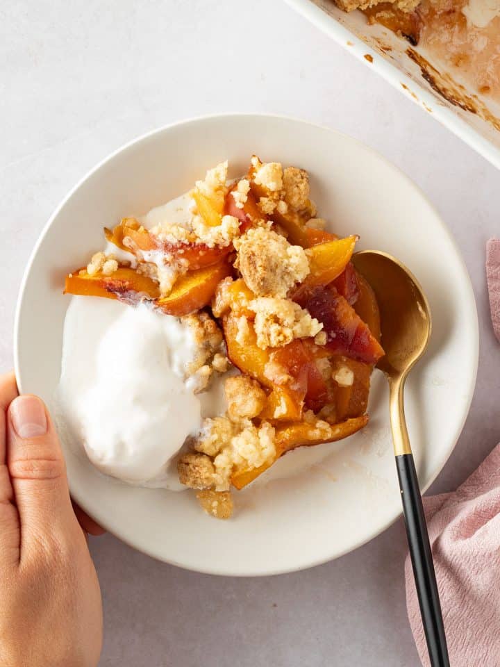 Eine Portion Obst Crumble auf einem Teller mit Vanilleeis, restlicher Crumble im Bildrand.