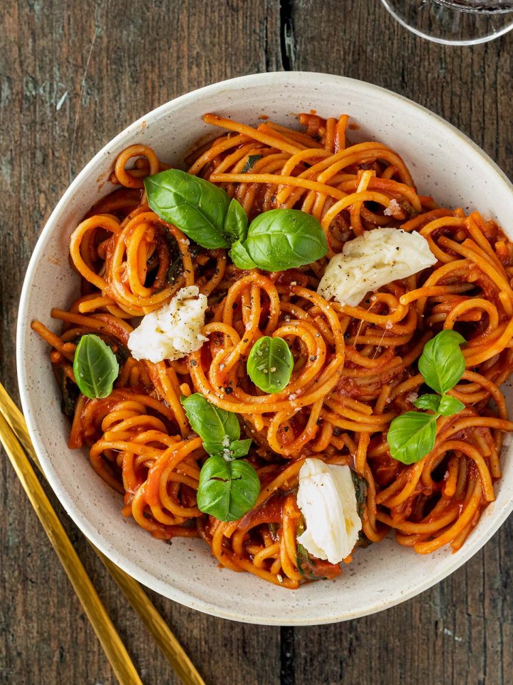 Teller Spaghetti in Tomatensauce mit frischem Mozzarella und Thunfisch auf einem Holzuntergrund.