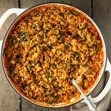 Orzo Pfanne mit Hackfleisch und Spinat auf einem dunklen Holzuntergrund.